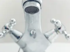 Gouttes d'eau tombant d'un robinet chromé. Comprendre la différence entre mitigeur et mélangeur pour une meilleure gestion de l'eau.