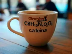 Taza de café blanca con la fórmula química de la cafeína y el texto "cafeína" impresos.