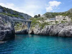 Ponte moderno su un mare cristallino, incastonato tra scogliere rocciose. Un luogo magico dove si incontrano i due mari in Puglia, con un ristorante panoramico sulla collina.