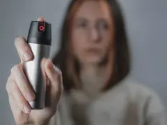 Dłoń trzymająca puszkę gazu pieprzowego na rozmytym tle.