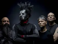 Quatre hommes, dont un avec un maquillage facial blanc et une crête, posent pour une photo. Le groupe Static X semble prêt à monter sur scène.