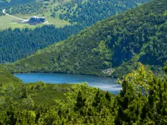 Widok na górskie jezioro i schronisko Samotnia w Karkonoszach. Otoczone zielenią, lasem i skalistymi zboczami.