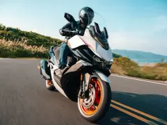 Kymco Xciting 400i dane techniczne: skuter z kierowcą na krętej drodze, z widokiem na góry i jezioro w tle.