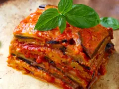 Una fetta di parmigiana di melanzane, stratificata e succulenta, guarnita con basilico fresco.