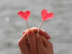 Dos piruletas rojas en forma de corazón, sostenidas por manos entrelazadas, como un símbolo de amor y una **venus carta astral**.