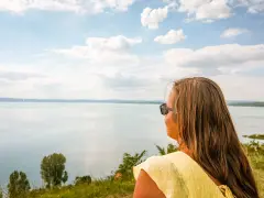 Kobieta w żółtej bluzce podziwia rozległe jezioro Balaton.