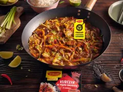 Kurczak w pięciu smakach po chińsku w woku, z warzywami i ryżem w tle. Obok limonki, chili i czosnek.