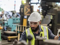Obrero con casco y gafas de seguridad trabajando en una máquina en una fábrica, parte esencial de la manufactura moderna.