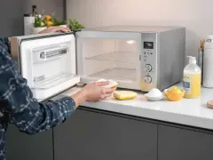 Une personne nettoie un mini four très encrassé avec une éponge. Des citrons, du bicarbonate et du liquide vaisselle sont à proximité.