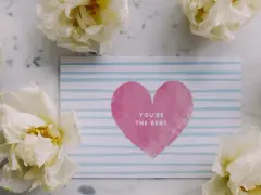 Kartka z sercem i napisem "You're the best" otoczona białymi kwiatami. Idealne komplementy dla mamy.
