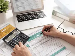 Ręce wypełniające formularz PIT-37, obok kalkulatora z wynikiem 236.12, laptopa i okularów.