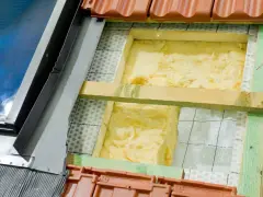 Wełna mineralna to świetny wybór, czym najlepiej ocieplić dom. Widoczna jest jej instalacja pod dachówką.