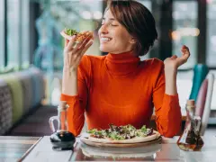 Kobieta w pomarańczowym golfie cieszy się pizzą, czując radość. W czym jest serotonina? W takich chwilach szczęścia!