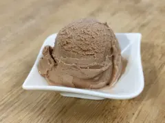 Ein Löffel cremiges Nougat Eis in einer weißen Schale auf einem Holztisch.