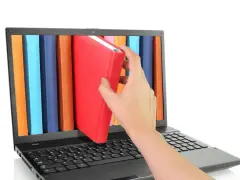 Mano saca un libro rojo de una estantería digital en una laptop. Acceso a información y al libro de IVA.