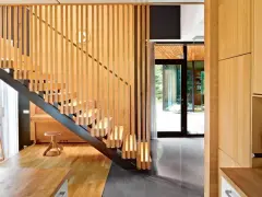 Nowoczesny stopień z drewna i metalu, z pionowymi drewnianymi balustradami. Obok fortepian i lampa.