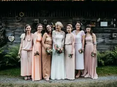 Brautjungfern in zarten Pastelltönen posieren vor rustikaler Holzwand, ein Bild von einer entspannten boho hochzeit.
