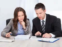 Dos profesionales concentrados revisan documentos y utilizan una calculadora para contabilizar facturas de años anteriores.