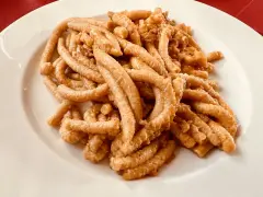 Pici all'aglione, uno dei piatti tipici di Arezzo, serviti su un piatto bianco.