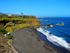 Spiaggia di sabbia nera e scogliere verdi sulle isole delle Canarie, con il blu intenso dell'oceano Atlantico.