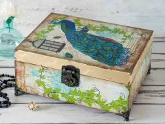 Ozdobna szkatułka z pawiem, klatką i liśćmi. To przykład techniki decoupage, która pozwala na piękne zdobienie przedmiotów.