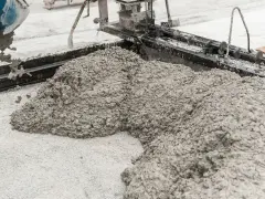 Beton wylewany z betoniarki na podłoże z drobnego kruszywa. Widać formę do wylewania betonu i masę, która tworzy kopiec.
