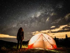 Nuit étoilée sur un bivouac GR34. Une personne admire la Voie lactée près d'une tente illuminée.