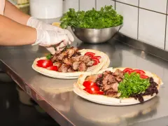 Ręce w rękawiczkach układają mięso na plackach z pomidorami i zieloną sałatą. Pyszny kebab gemuse gotowy do podania.