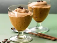 Due bicchieri di spumone al caffè, guarniti con chicchi di caffè, su un tavolo verde.