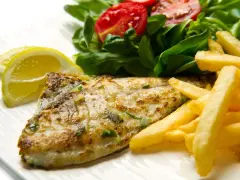 A cooked fish fillet with french fries, salad, and lemon slices on a white plate.