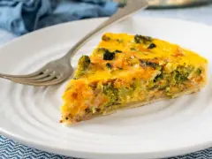 Rebanada de quiche vegetal con brócoli y zanahoria, servida en plato blanco con tenedor.