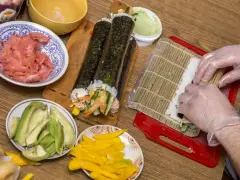 Przygotowanie domowego sushi: ryż, awokado, mango, imbir i rolki w trakcie zwijania.