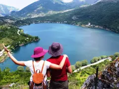 Coppia ammira un lago a forma di cuore, circondato da montagne verdi e alberi.