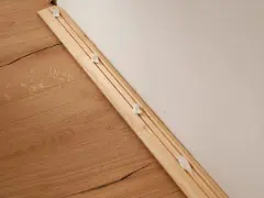 Drewniana listwa przypodłogowa z widocznymi klipsami montażowymi, gotowa do instalacji na podłodze.
