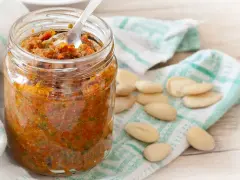Vasetto di pesto di pomodori secchi, con mandorle sparse su un canovaccio.