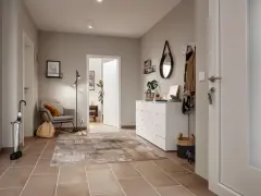 Stilvoller Flur gestalten: Grauer Sessel, Teppich, weiße Kommode mit Spiegel und Garderobe schaffen eine einladende Atmosphäre.