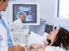 Lekarka pokazuje na monitorze USG obraz płodu, przyszła mama z uśmiechem czeka na wieści o płci.
