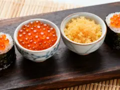 Dwa sushi rolki z pomarańczowym ikrą masago i miseczki z ikrą.
