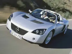 Srebrny Opel Speedster z dwoma pasażerami pędzi po krętej drodze.