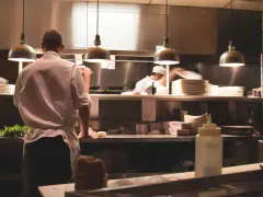 Kucharz w białej koszuli i fartuchu pracuje w kuchni restauracyjnej. To idealne miejsce, by napisać list motywacyjny kucharz.