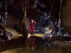 Eksplorator w jaskini, zanurzony po kolana w wodzie, oświetla drogę czołówką. To właśnie jest speleologia – odkrywanie podziemnego świata.