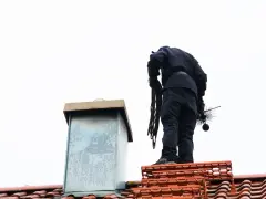Kominiarz na dachu z narzędziami. Zastanawiasz się, ile kosztuje czyszczenie komina? To ważna usługa dla bezpieczeństwa.