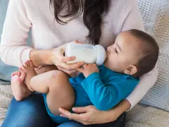 Mama karmi dziecko butelką. To przykład karmienia mieszanego, gdzie dziecko otrzymuje zarówno mleko matki, jak i mleko modyfikowane.