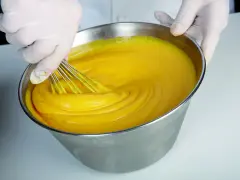 Mani guantate montano una crema pasticcera perfetta, come insegna Iginio Massari. La consistenza è vellutata e il colore giallo intenso.
