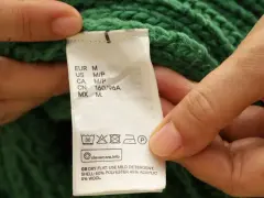 Etichetta di un maglione verde che indica il lavaggio in lavatrice a 30 gradi, con istruzioni per il lavaggio del cotone.