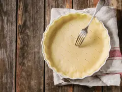 Pâte brisée sans beurre dans un plat à tarte, prête à être garnie. Une fourchette est plantée dans la pâte.
