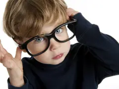 Chłopiec z niebieskimi oczami poprawia okulary, zastanawiając się nad nadwzrocznością u dzieci kiedy okulary są potrzebne.