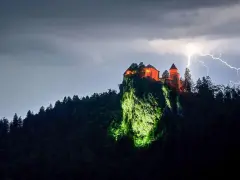 Zamek Poenari, oświetlony na czerwono, góruje nad skalistym zboczem podczas burzy z piorunami.
