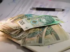 Stos banknotów 100 zł na dokumentach. Czy to wystarczy na najniższą emeryturę?