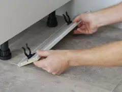 Mani che assemblano uno zoccolo cucina in alluminio, mostrando come tagliare e fissare i supporti.